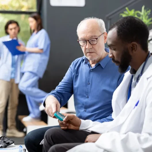 Healthcare worker performs routine blood sugar testing on senior white man using glucometer. The medical checkup supports early diagnosis and healthy lifestyle monitoring in clinic waiting room.