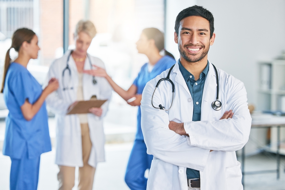 Two men and two women in lab coats with stethoscopes sitting at table and using modern gadgets, afro lady giving papers for colleagues. Multiracial doctors analyzing diagnosis of severe patient.